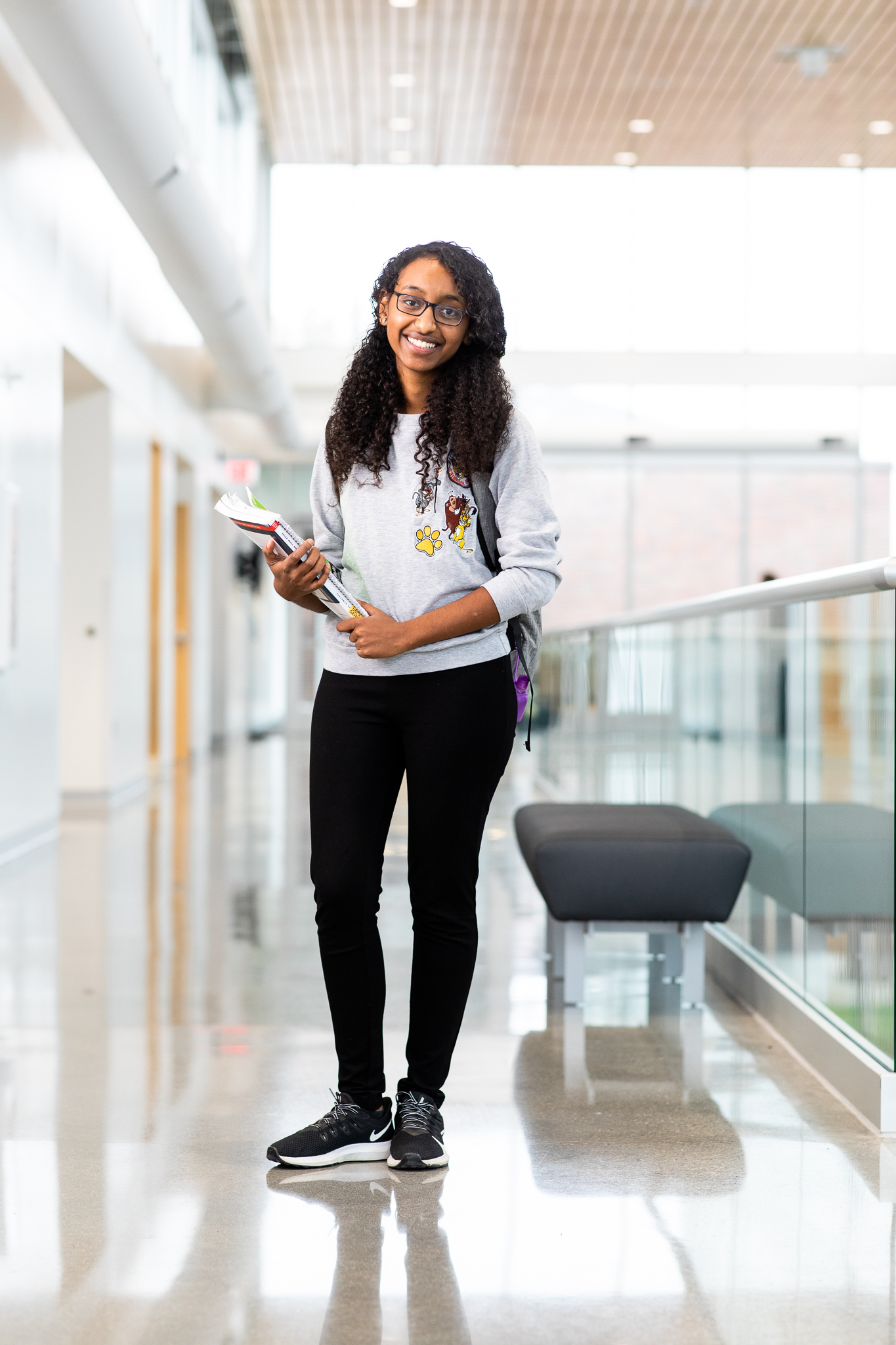 Saron Gebre wearing a gray sweater and black pants, standing while elegantly holding books in her arms.